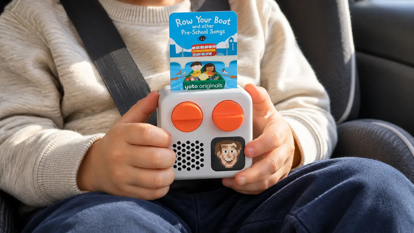 A preschooler in a car seat holding a Yoto Mini with a song card in it